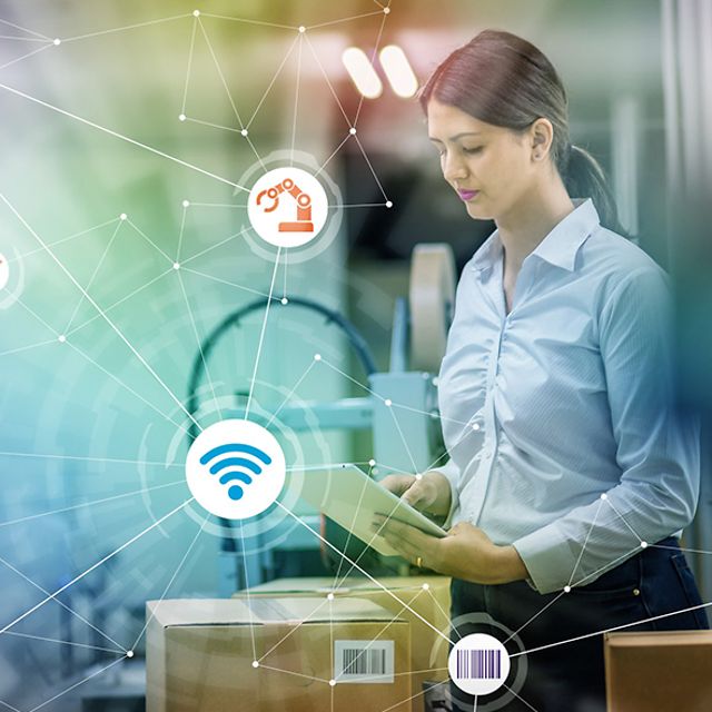 A woman looking at a tablet in a warehouse with packages.