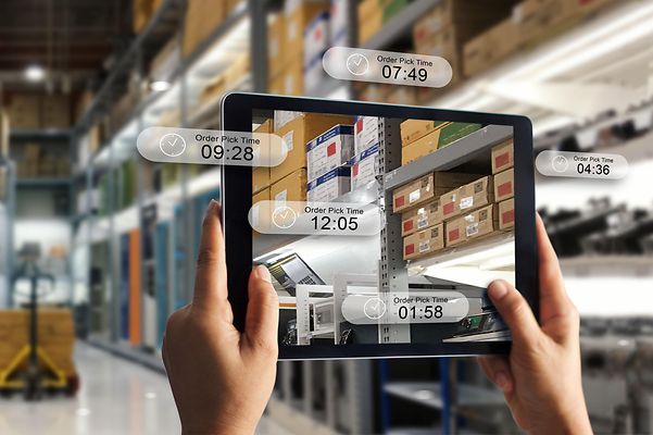 A warehouse with shelves full of boxes and a tablet in the foreground that shows an augmented reality interface.