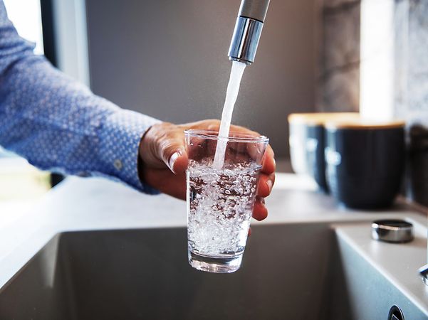 Mensch füllt Glas mit Wasser aus Wasserhahn