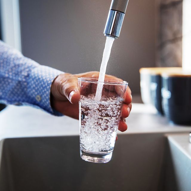 Mensch füllt Glas mit Wasser aus Wasserhahn