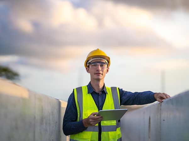 Mann mit Sichereitsweste und Helm hält ein Tablet in der Hand.
