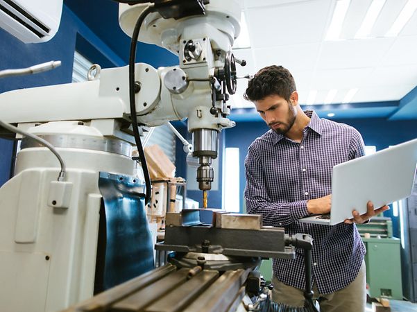 Mann der mit Laptop eine Maschine bedient