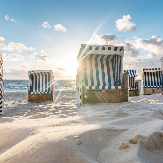 Beach chairs on sand with the sea and blue sky in the background.