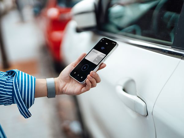 Close-up of a young woman unlocking her car using a mobile phone app on her smartphone.