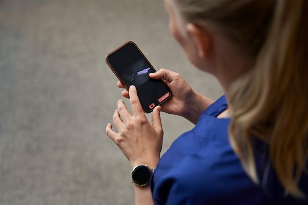 Frau in Pflegeuniform hält Smartphone und tippt mit Fingern