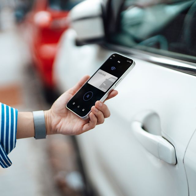 Close-up of a young woman unlocking her car using a mobile phone app on her smartphone.