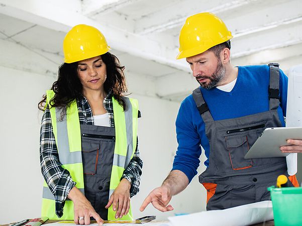 Woman and man studying building plans on a tablet in a building shell
