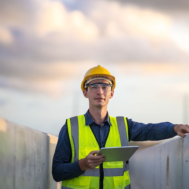 Man with safety waistcoat and helmet holding a tablet.