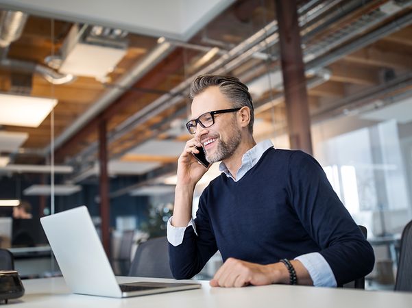 En affärsman som pratar i telefon medan han arbetar på en bärbar dator på ett modernt kontor.