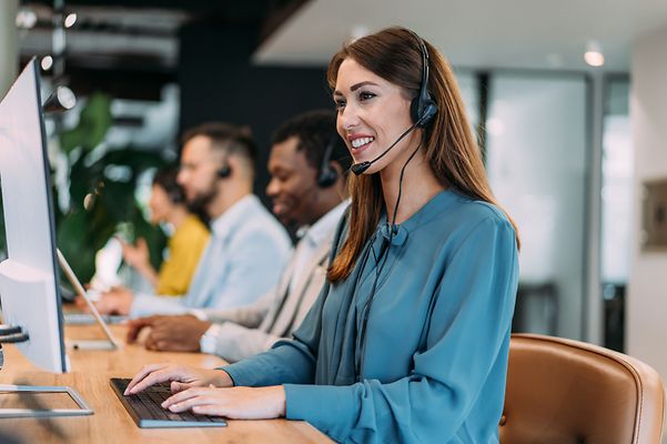Una mujer con auriculares, sentada en un escritorio y sonriendo.