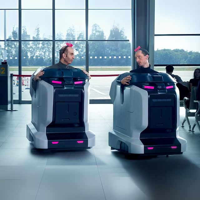 Personas con trajes de robot aspirador en el vestíbulo de un aeropuerto.
