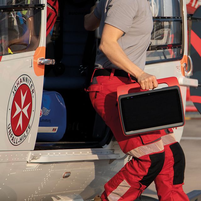 A paramedic carries a rugged tablet as he steps out of a rescue helicopter.