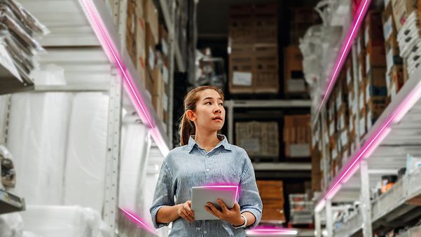 Eine Frau nutzt den Low Cost Tracker im einem Lager mit hohen Regalen und magentafarben beleuchteten Gängen.