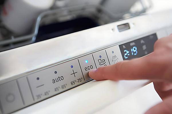 Finger tippt auf Eco-Modus einer Spülmaschine zur Energieeinsparung.