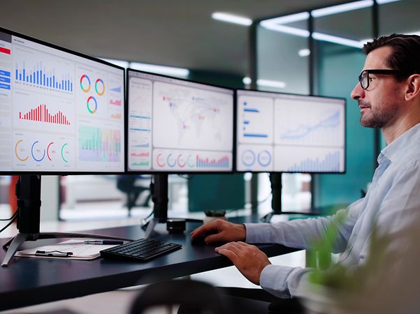 Mann am Schreibtisch mit drei Monitoren, die Diagramme und Grafiken des M2M Service Portals zeigen