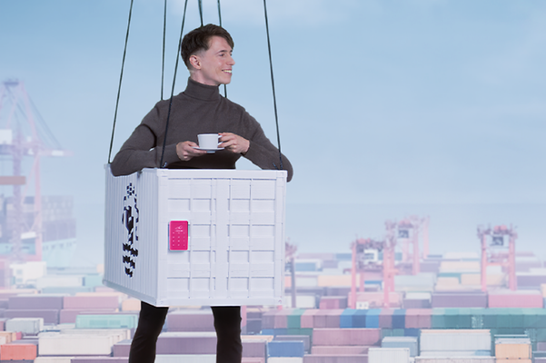 Ein Mensch steckt in einem Container Kostüm und hängt vor einem Hintergrund, der einen Container-Hafen darstellt.
