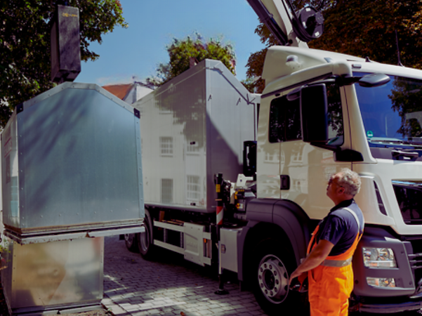 Ein Mitarbeiter der Müllabfuhr bedient den Kran eines LKWs um einen Glascontainer zu entleeren