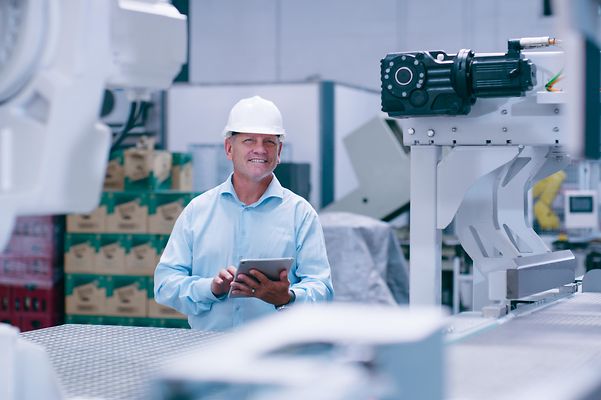 Mann mit Sicherheitshelm hält Tablet in einer Produktionhalle.